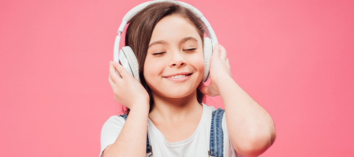 Girl listening to music with headphones on against pink background