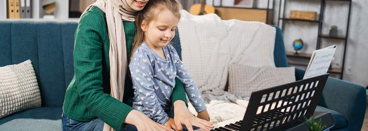 Girl and her mother are playing piano together at home