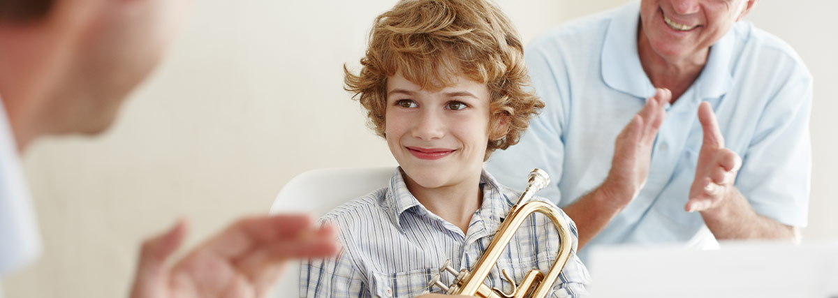 Two men clapping with smile to boy with trumpet