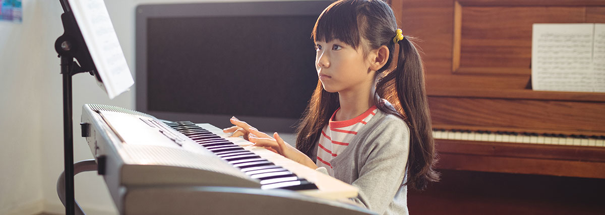 Girl playing piano by looking at music paper