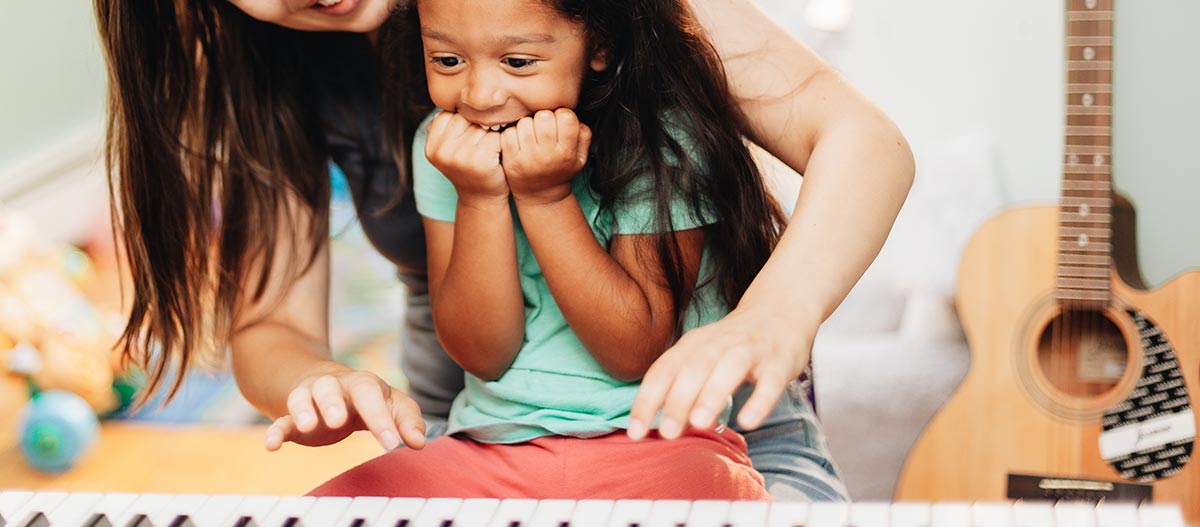 Girl smiling to play piano with woman