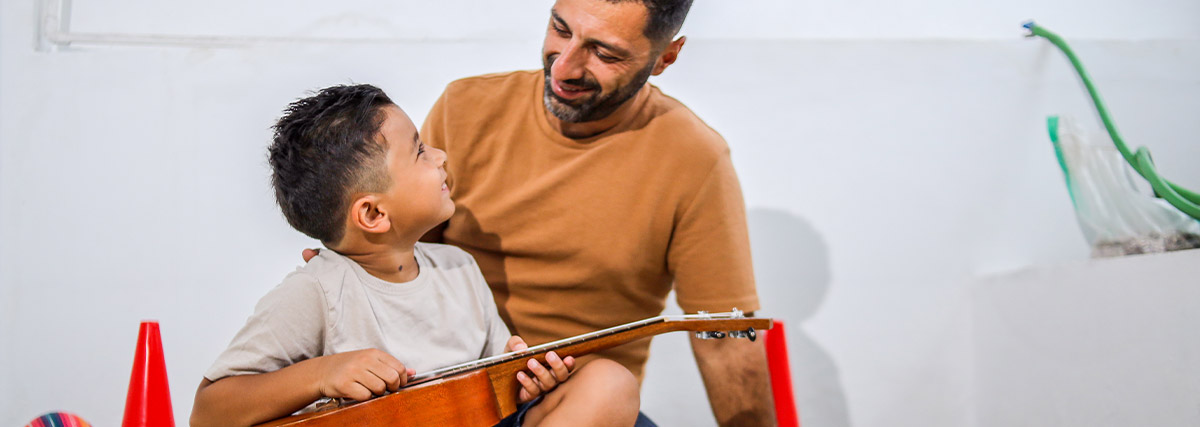 Parent encouraging a child holding a guitar, supporting confidence and cognitive flexibility through music