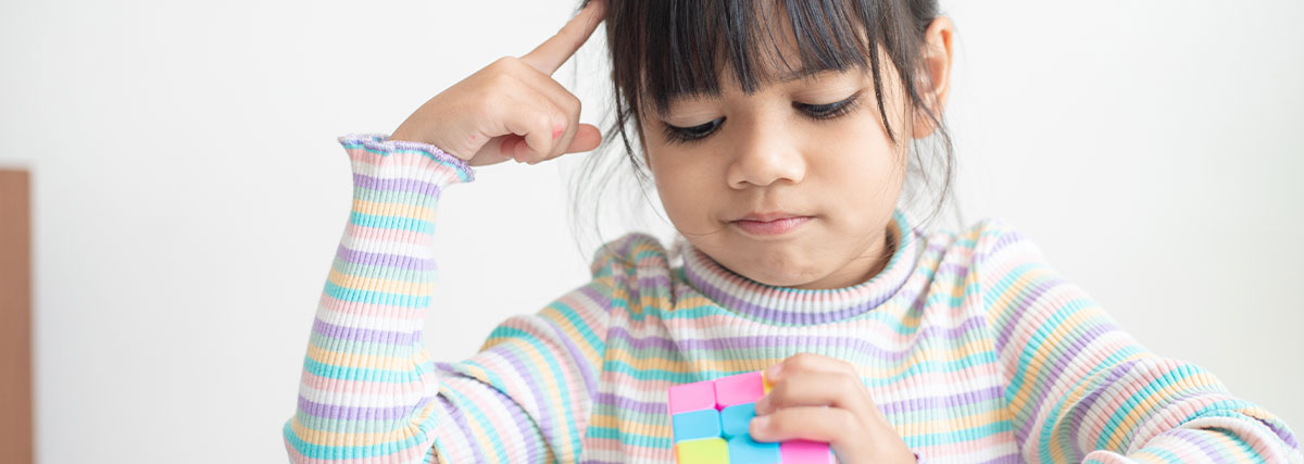 Young girl solving a colourful cube, puzzle, demonstrating concentration, problem solving and cognitive flexibility
