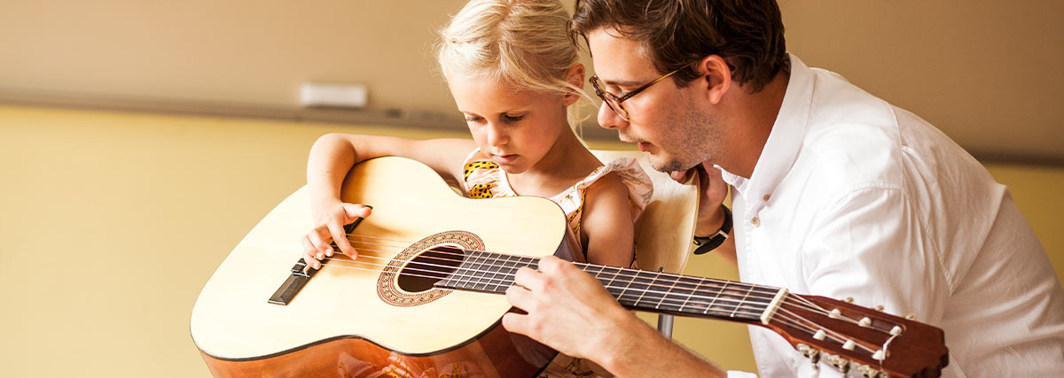 Young child learning guitar with supportive guidance from a music teacher
