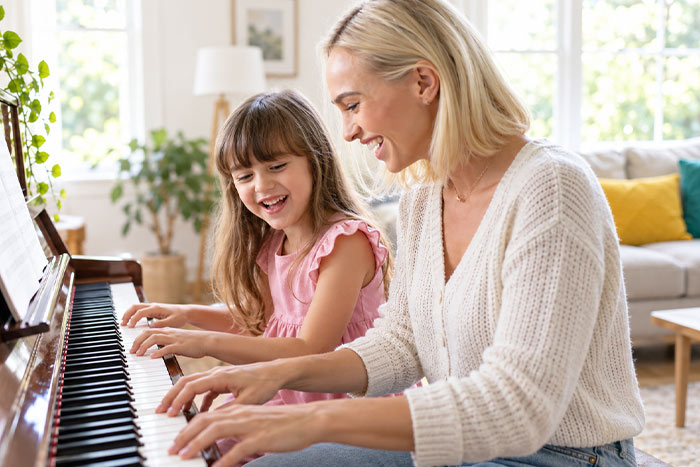 Mother and daughter happily playing piano together at home