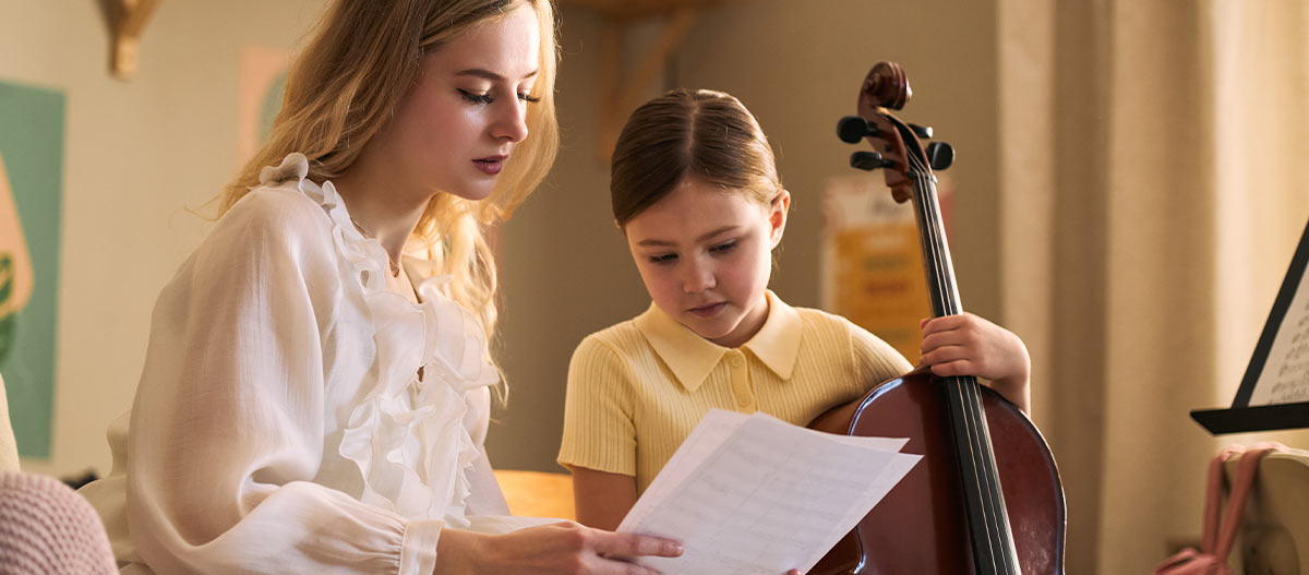 Young cello student choosing sheet music with guidance from her teacher