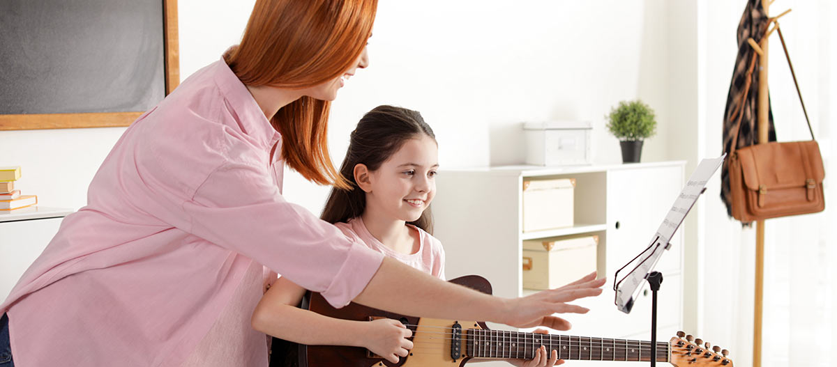 Young girl enjoying a relaxed guitar lesson with a supportive music teacher